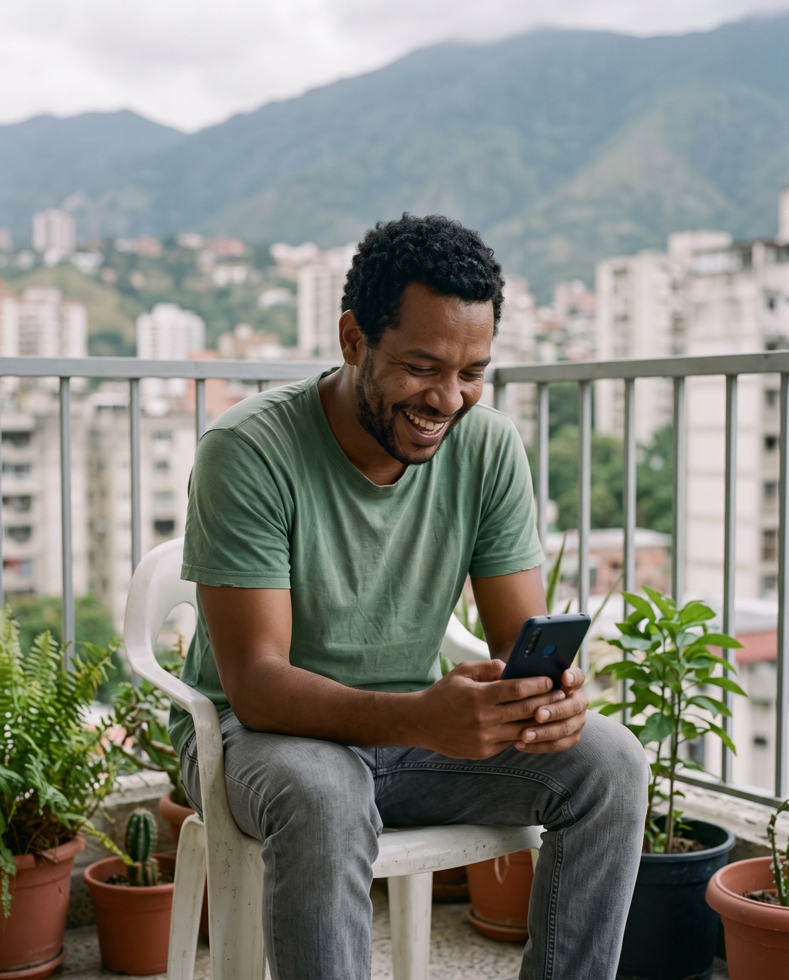 Un hombre se ríe con un mensaje en su teléfono, sentado en el balcón de su apartamento en Caracas.
