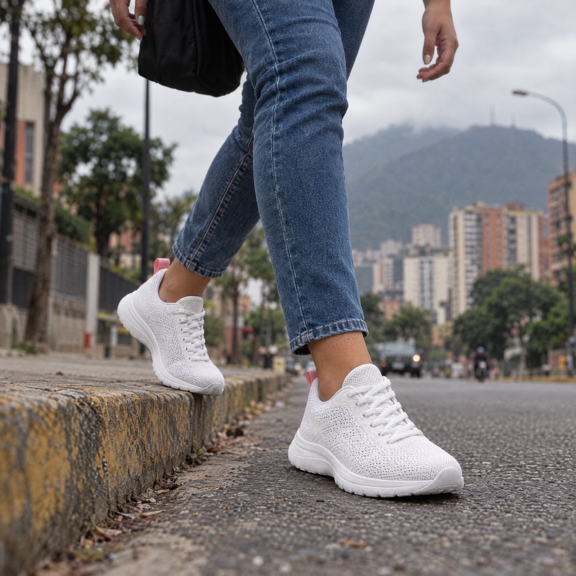 Una joven estrena sus zapatos de correr al bajar de la acera en una calle de Caracas, con El Ávila al fondo.